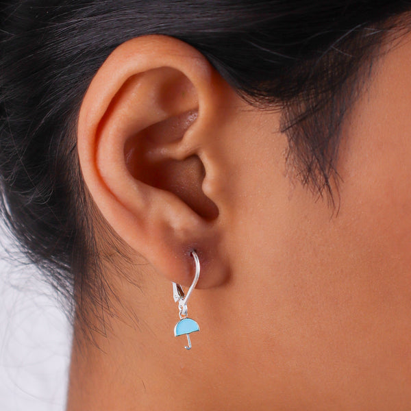Earrings worn by a woman showing silver enamel umbrella design