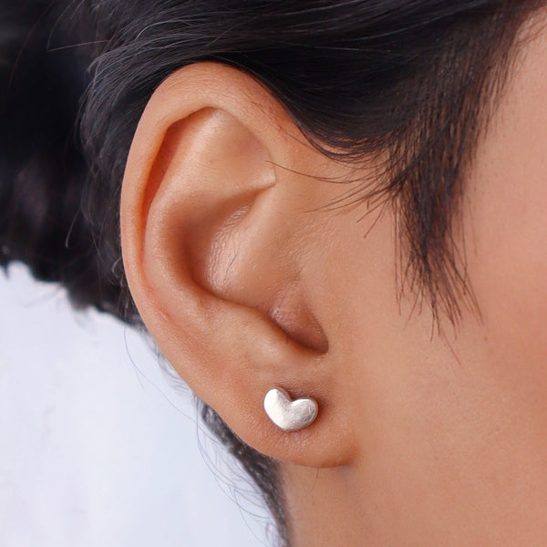Woman wearing silver heart stud earrings near ear