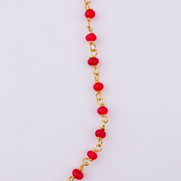 Red beaded necklace with gold chain on white surface