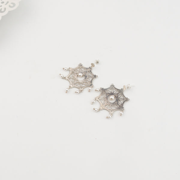 Silver filigree earrings with pearls on white surface