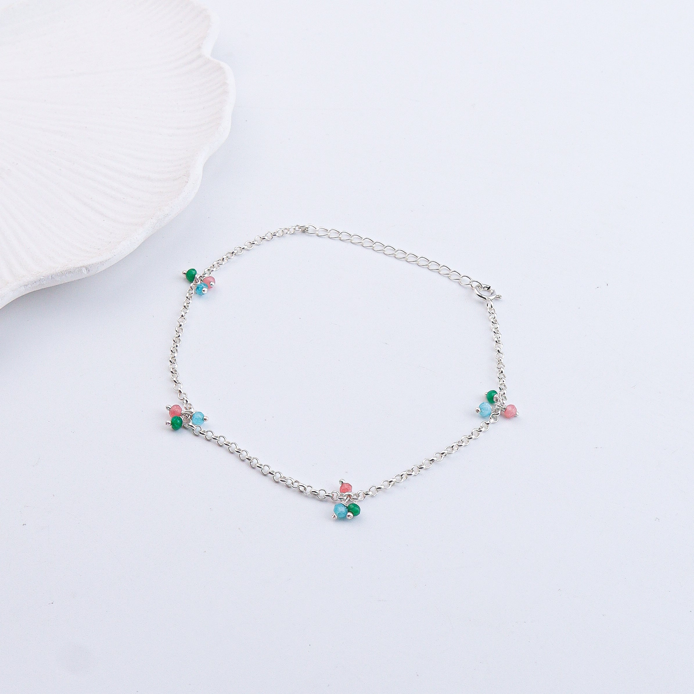 Close-up of silver anklet with beads on white surface