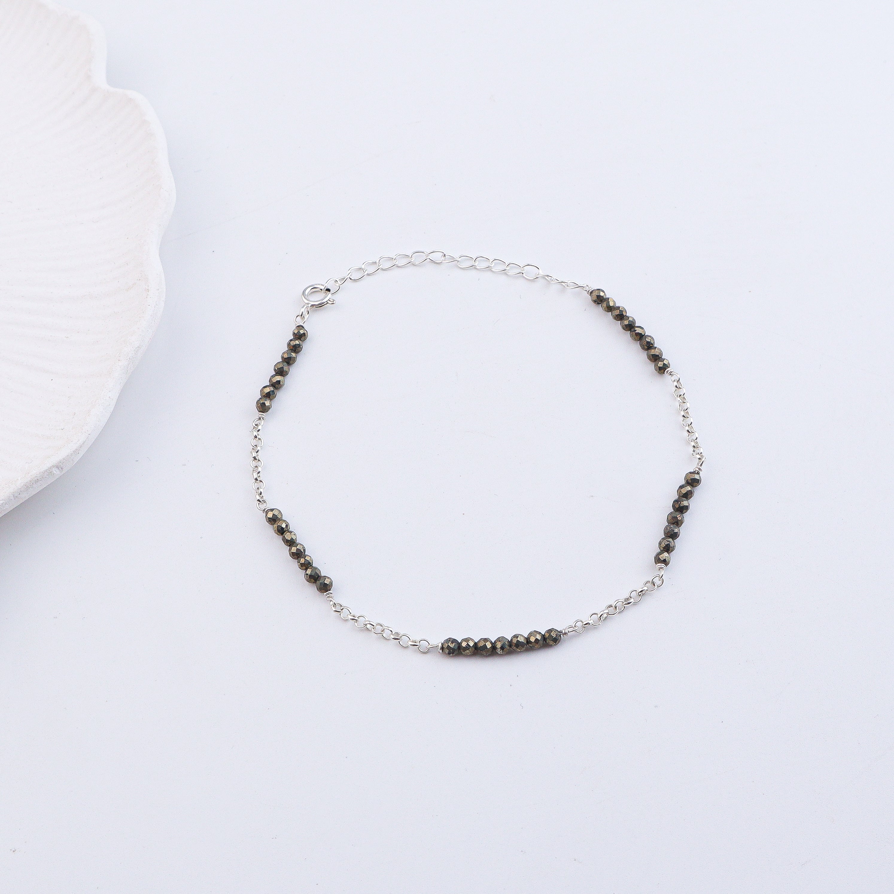 Silver and black beaded anklet on white fabric surface