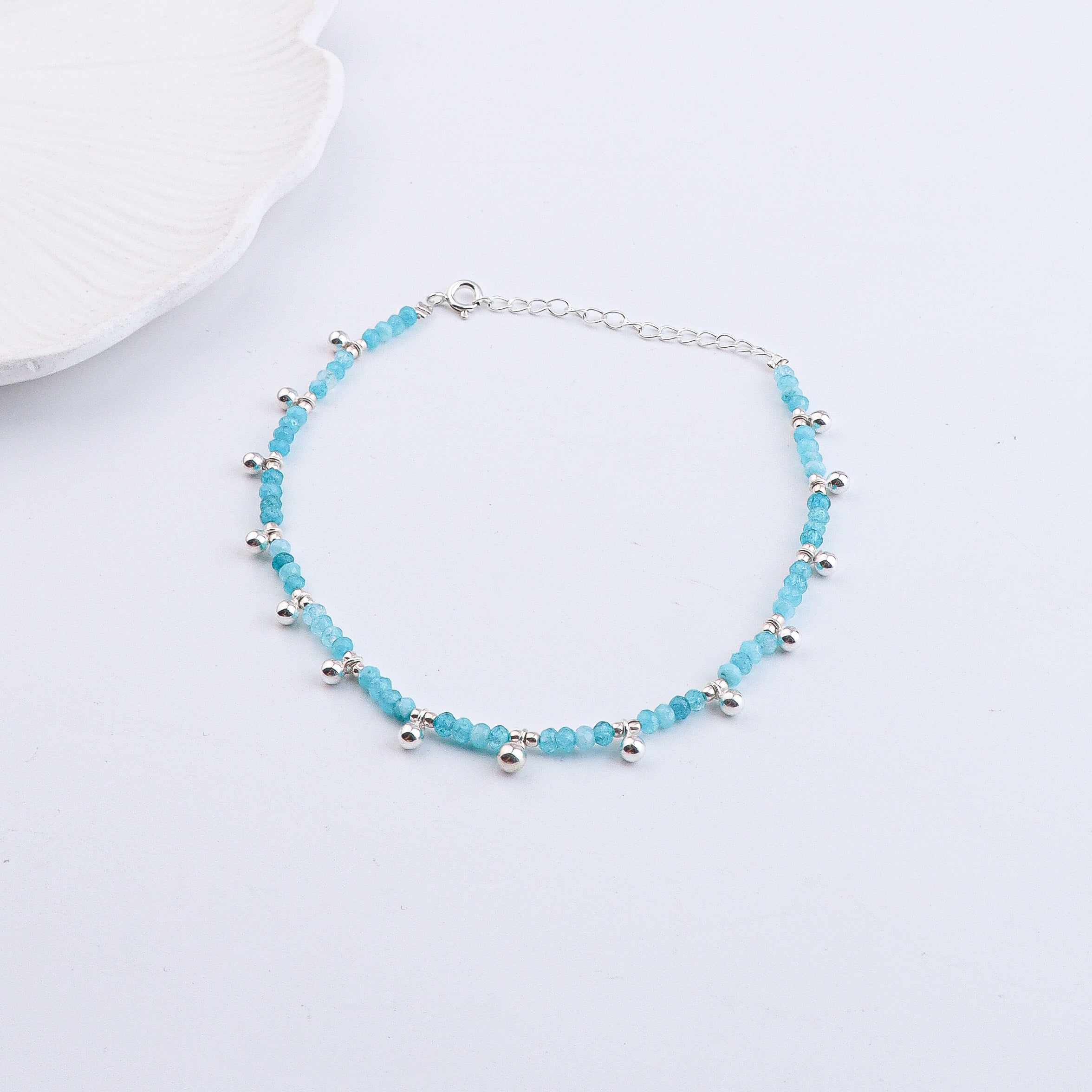 Silver and blue gemstone anklet displayed on white fabric