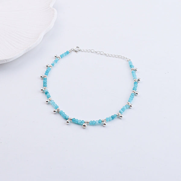 Silver and blue gemstone anklet displayed on white fabric