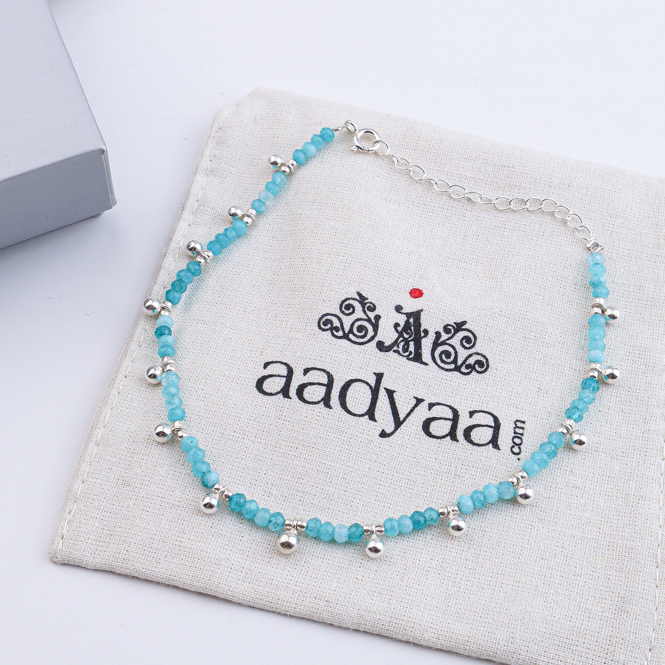 Silver and blue beaded anklet on white textured surface