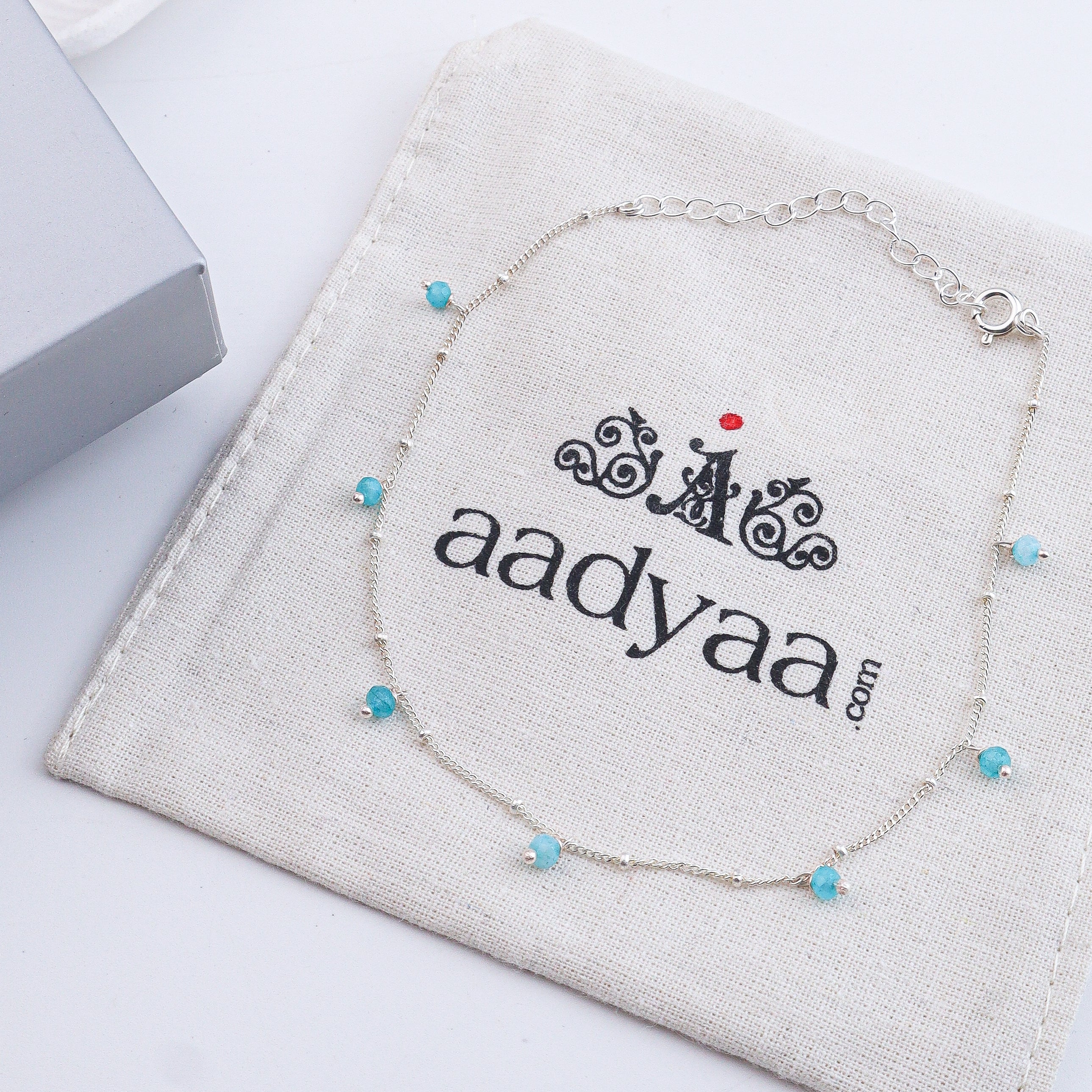 Close-up of silver anklet with blue beads on a white surface
