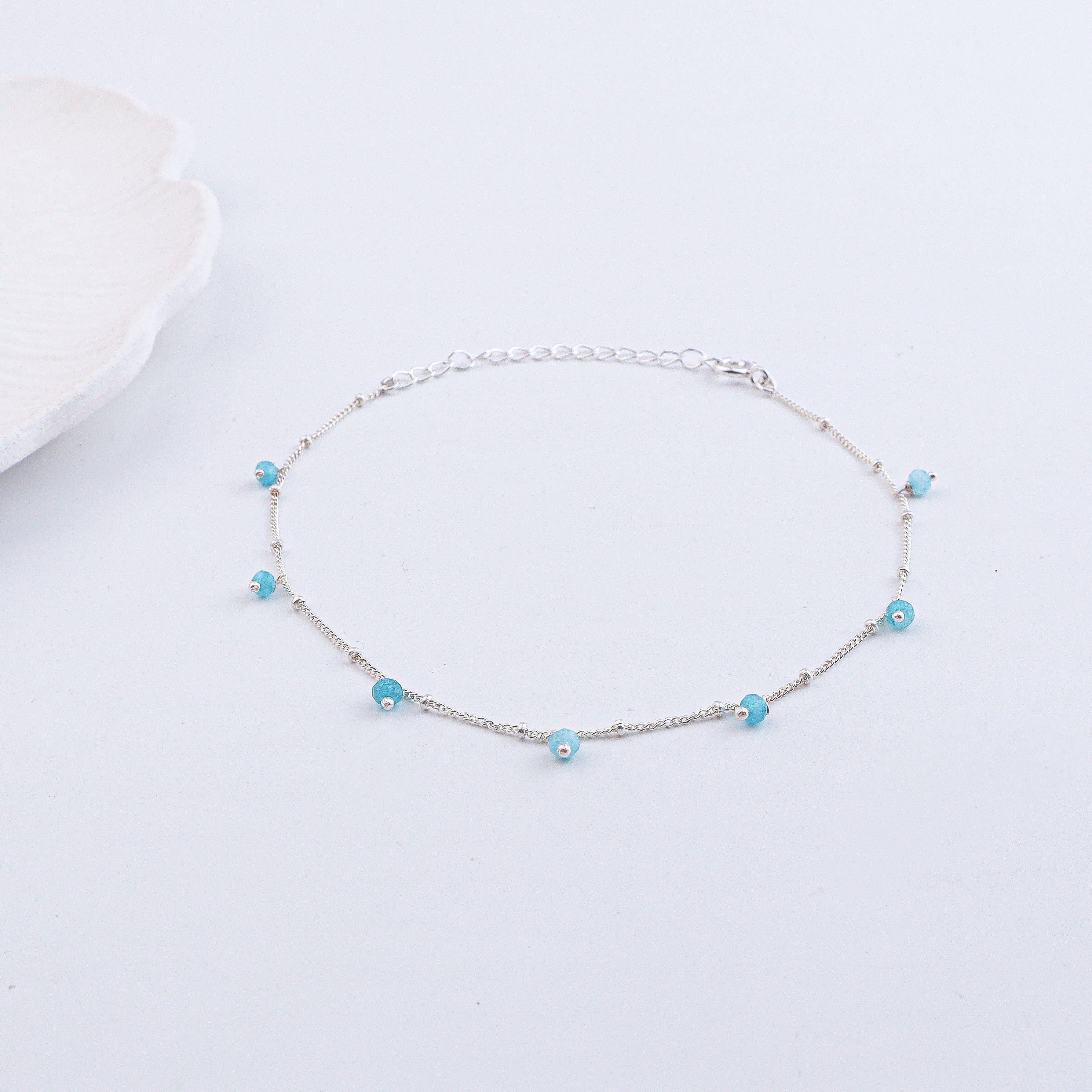 Silver anklet with blue beads on a white textured background