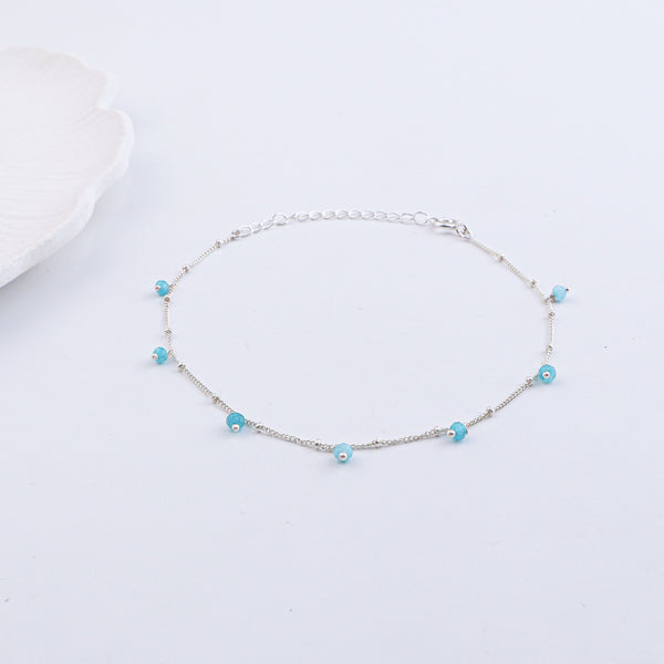 Silver anklet with blue beads on a white textured background