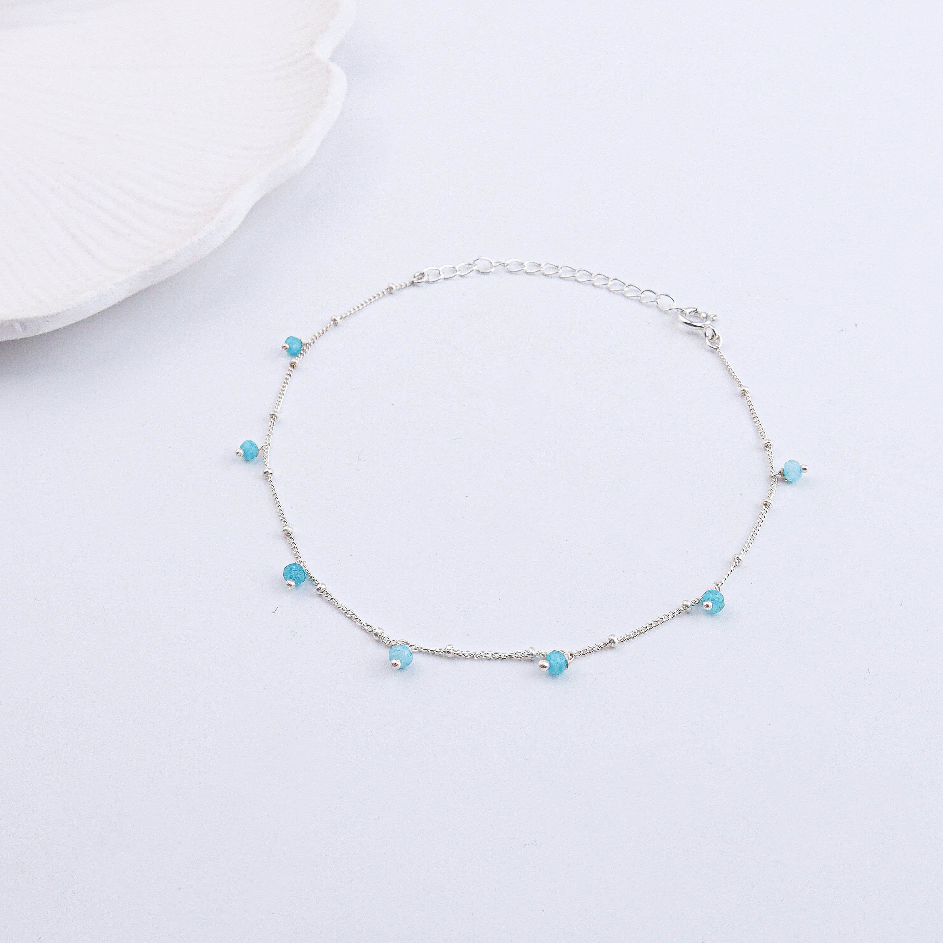 Silver anklet with blue beads on a white fabric with text