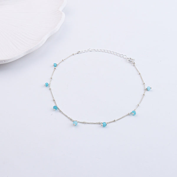 Silver anklet with blue beads on a white fabric with text