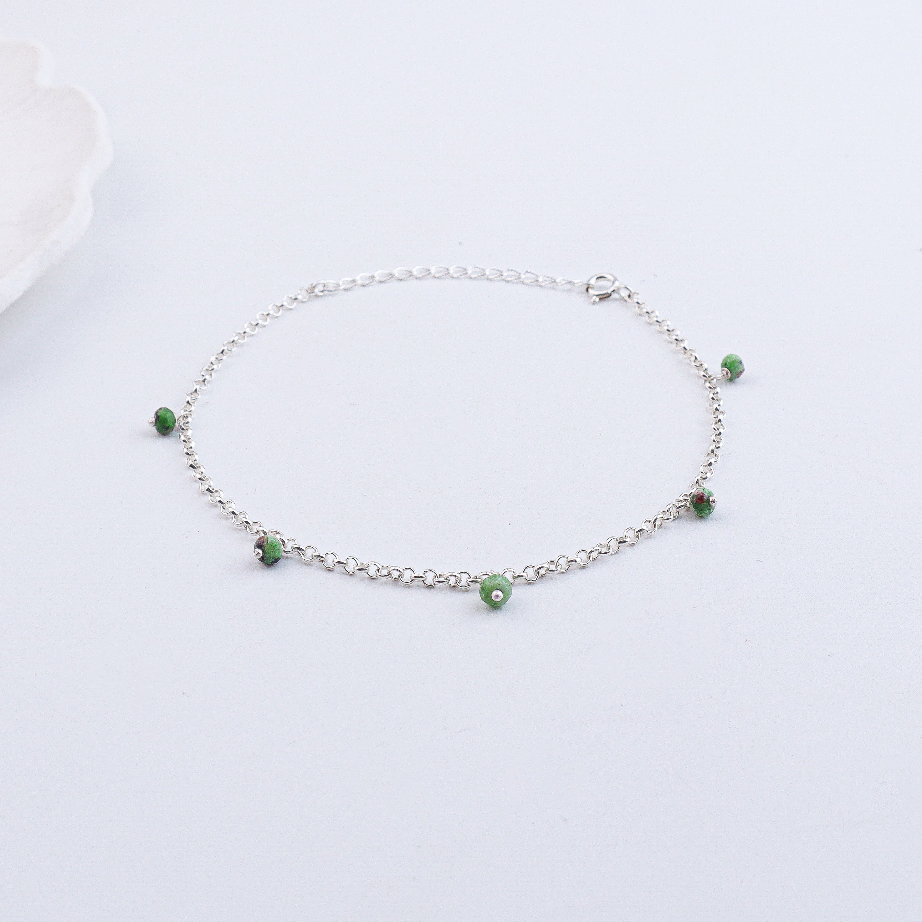 Silver anklet with green beads on white surface