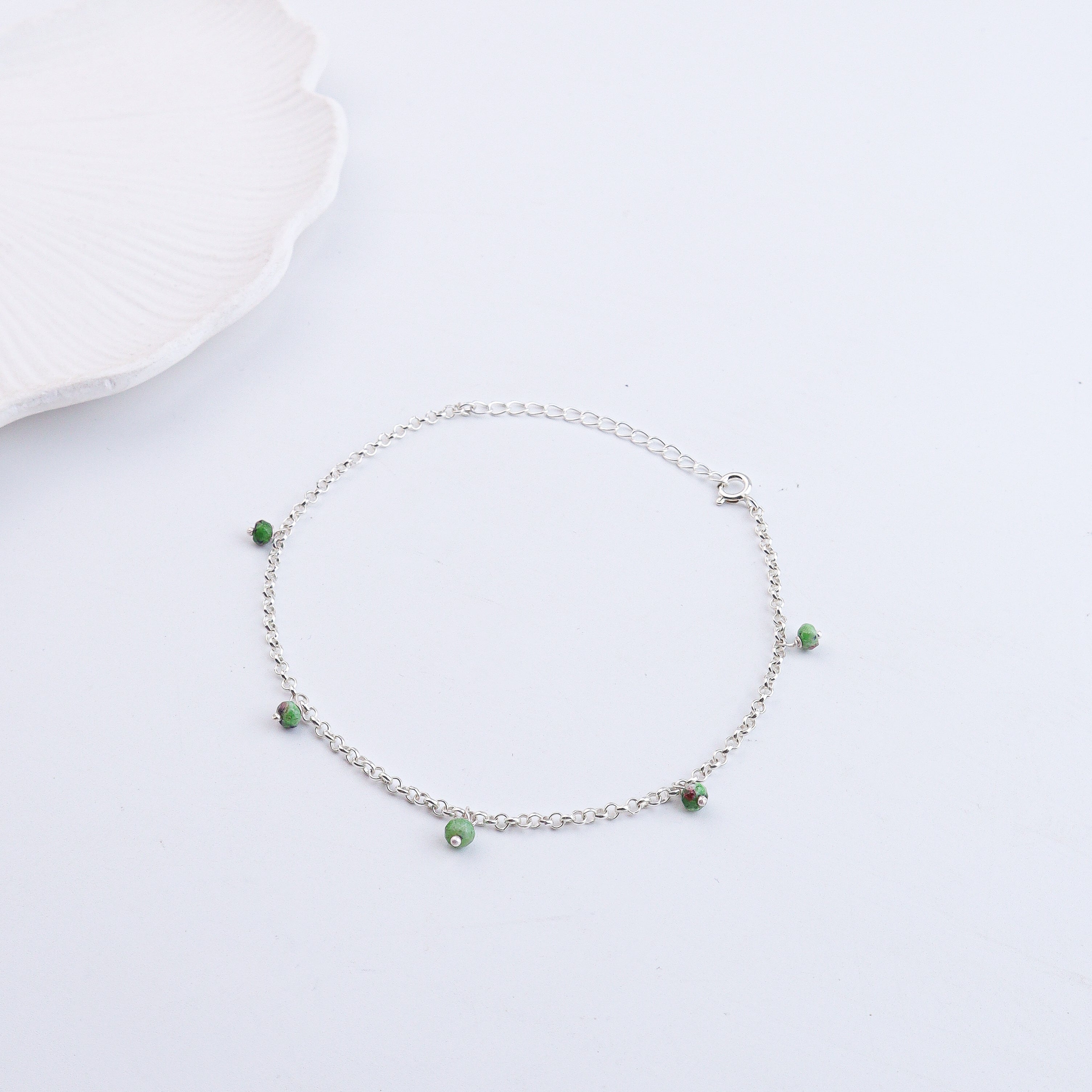 Silver anklet with green beads on white background