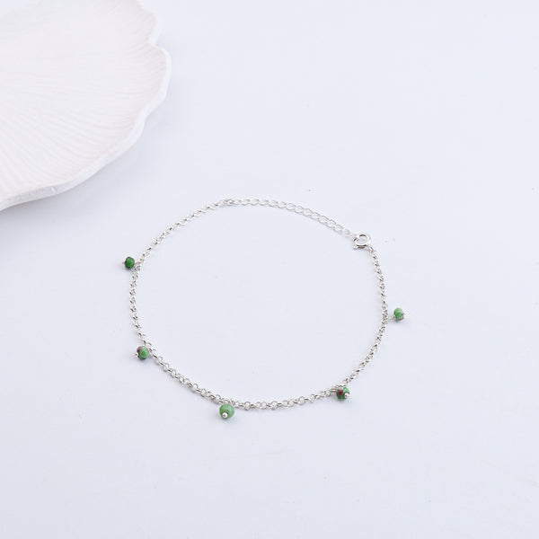 Silver anklet with green beads on white background
