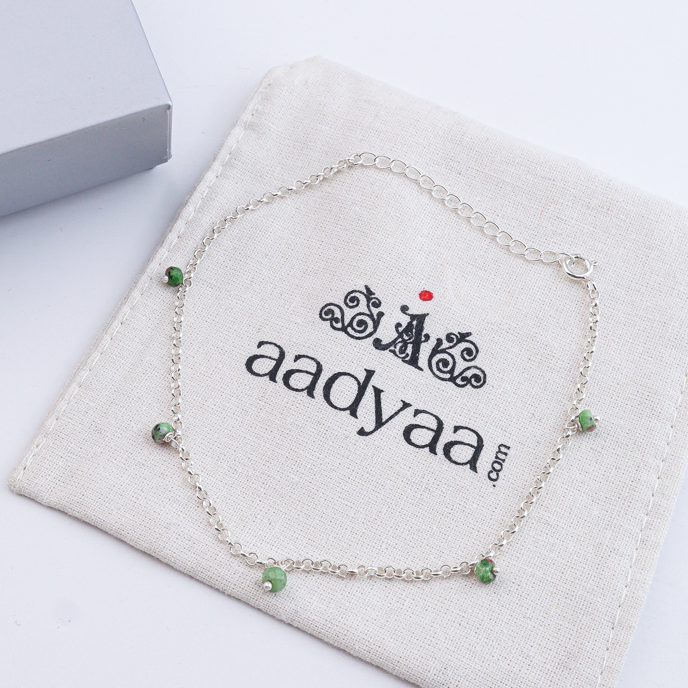 Silver anklet with green beads on white fabric