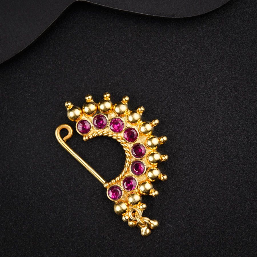 a gold brooch with pink stones on a black background