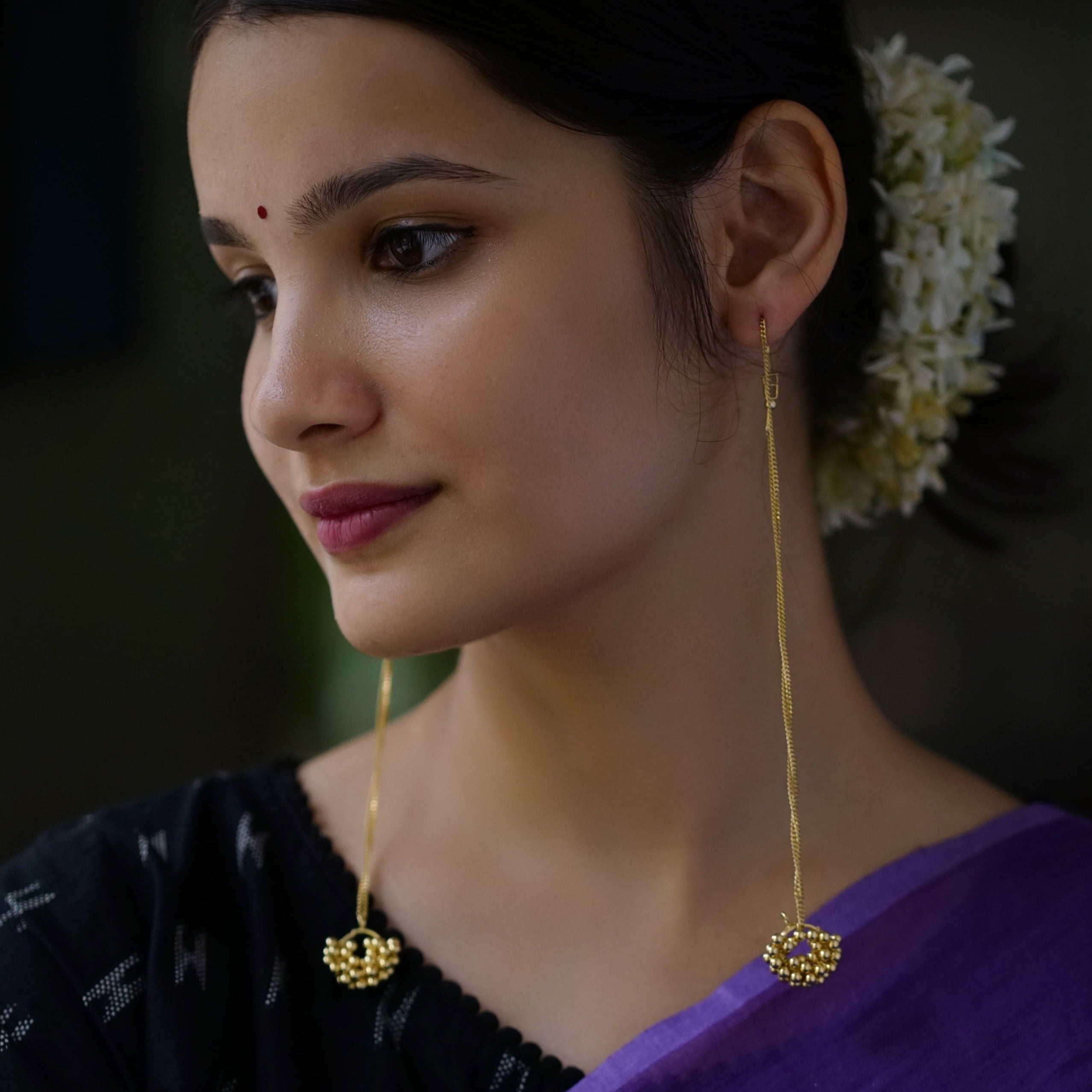 a woman wearing a purple saree and a pair of gold earrings
