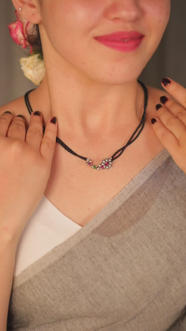 Elegant black beaded necklace with pink, green, and silver accents, worn by a woman with floral earrings