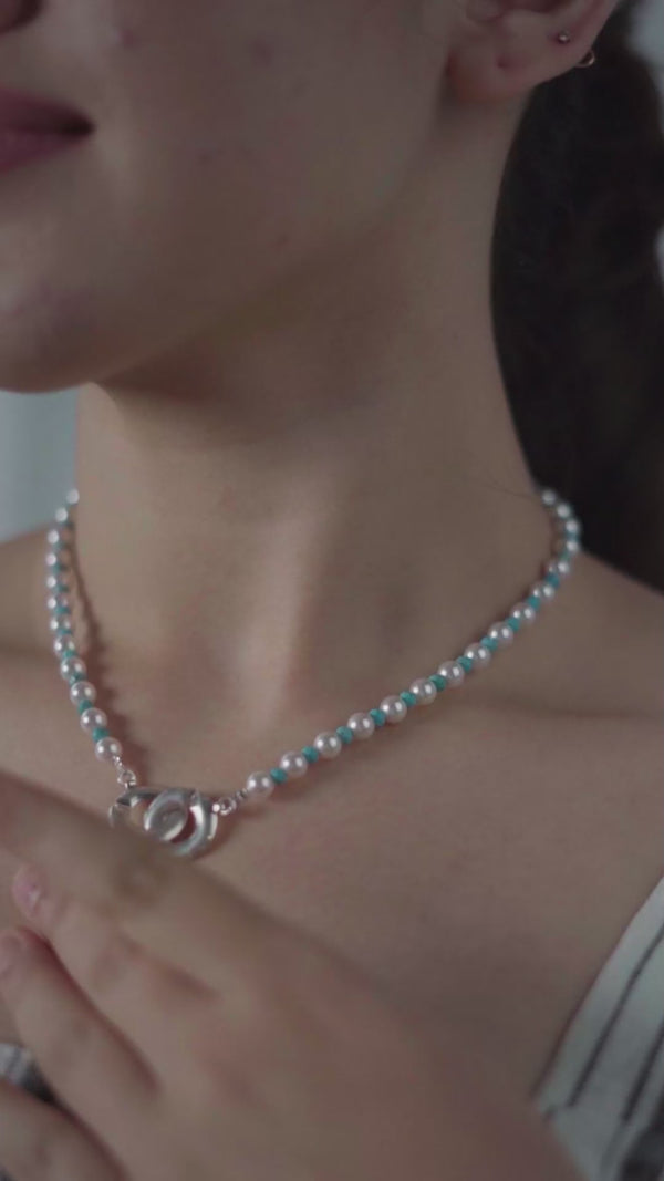 Pearl and turquoise infinity lock necklace on a woman's neck