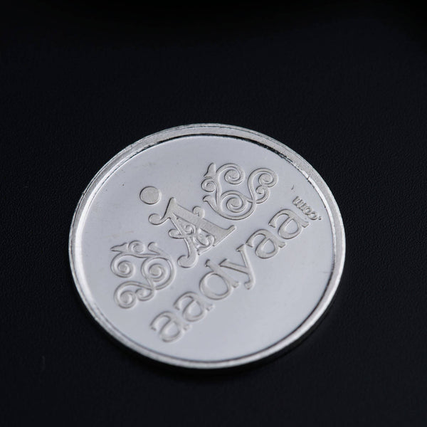 Silver diya and coin displayed on black background
