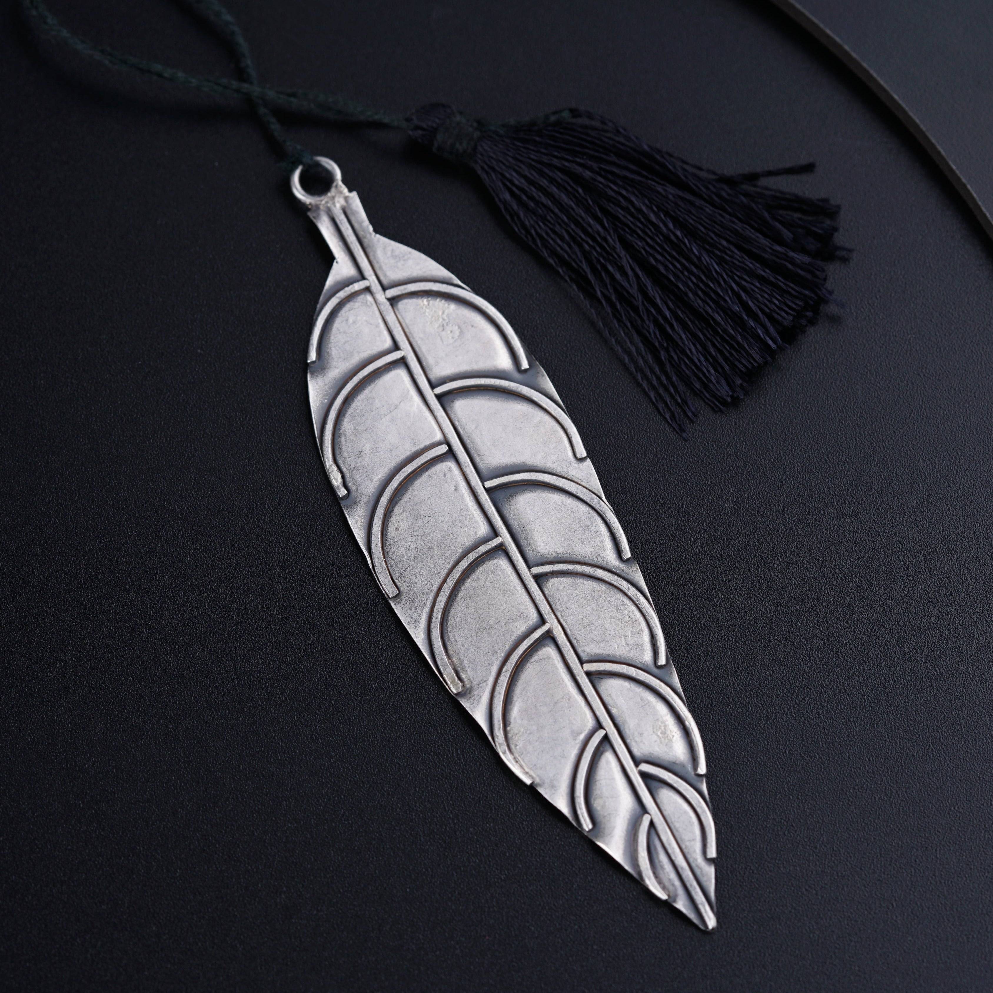 a silver feather pendant with a tassel on a black background