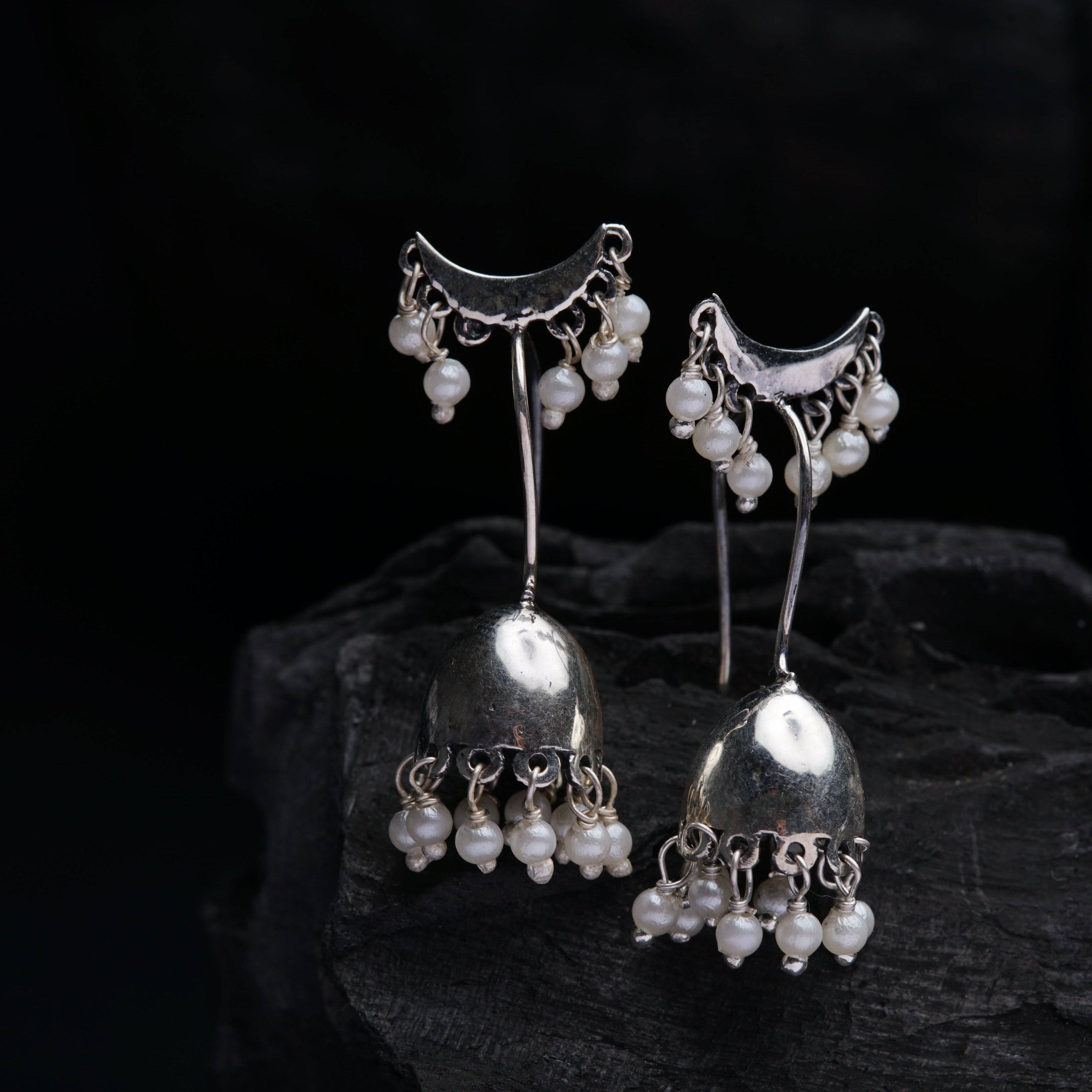 a pair of silver and pearl earrings on a rock