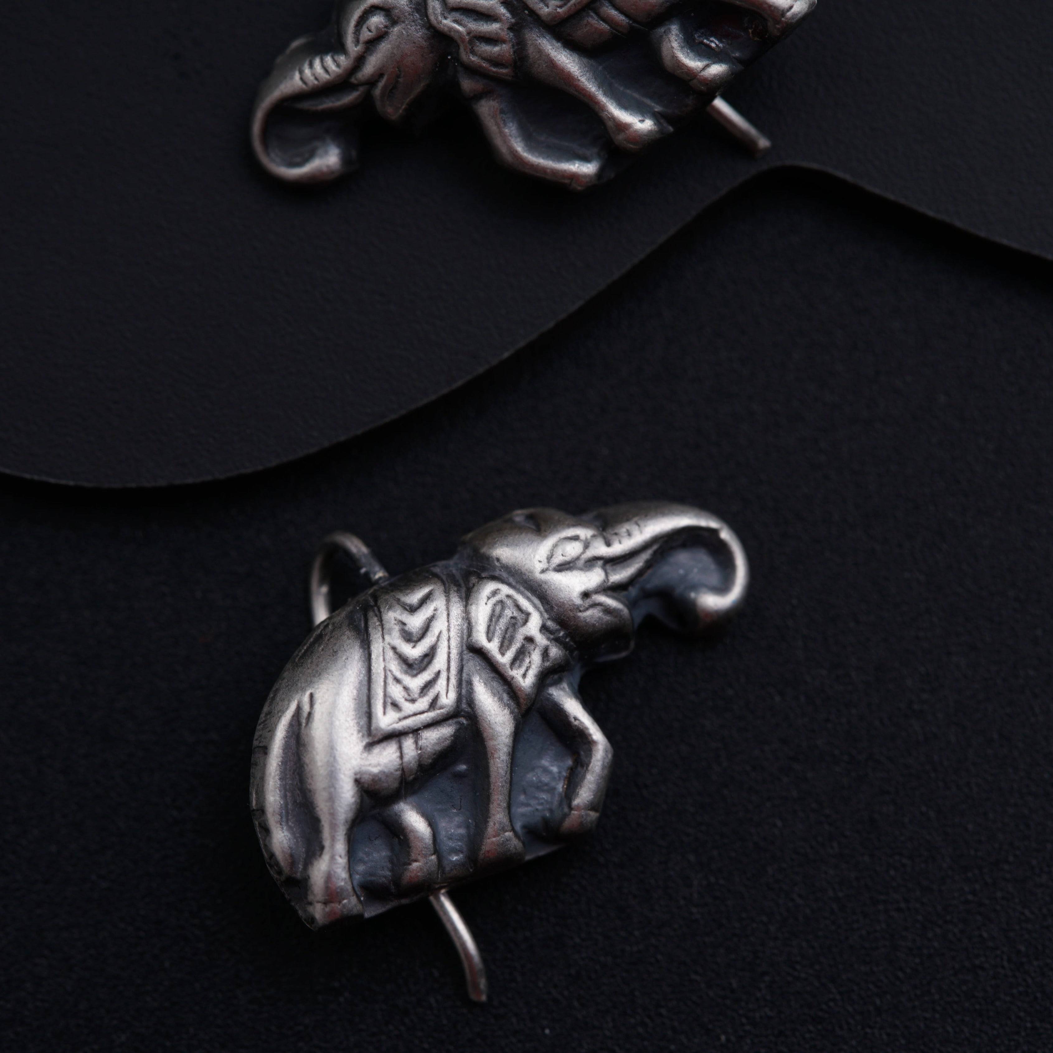 two silver elephant brooches sitting on top of a black surface