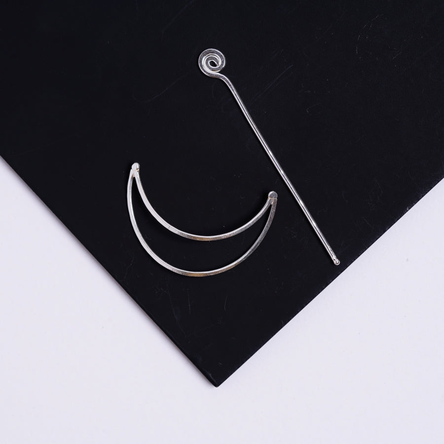 a pair of silver hoop earrings sitting on top of a black piece of paper