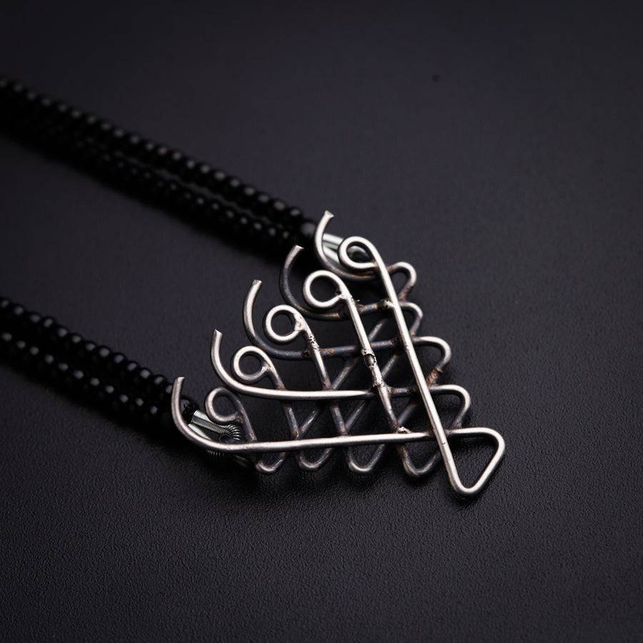 a silver pendant with a black cord on a black surface