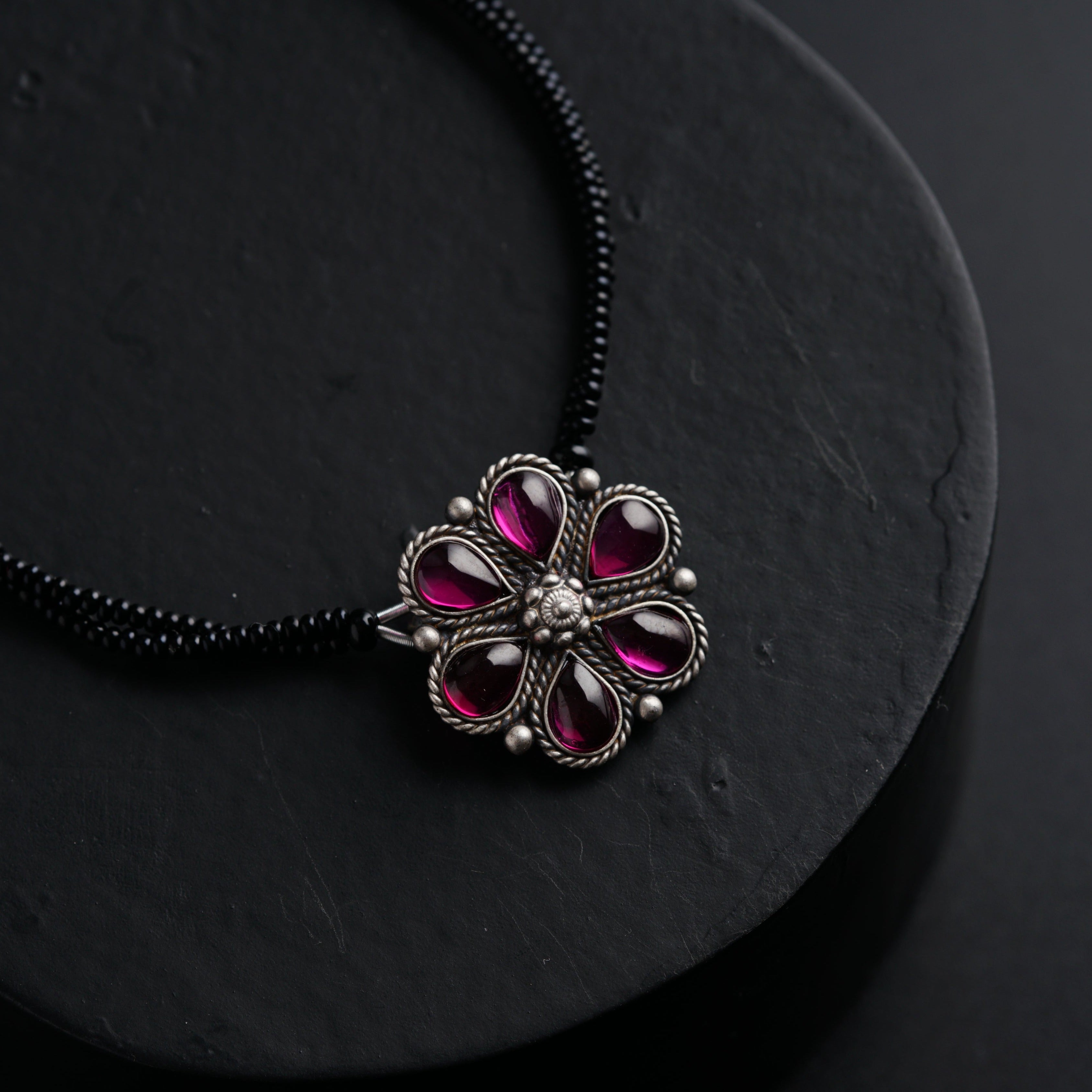 a black necklace with a pink flower on it