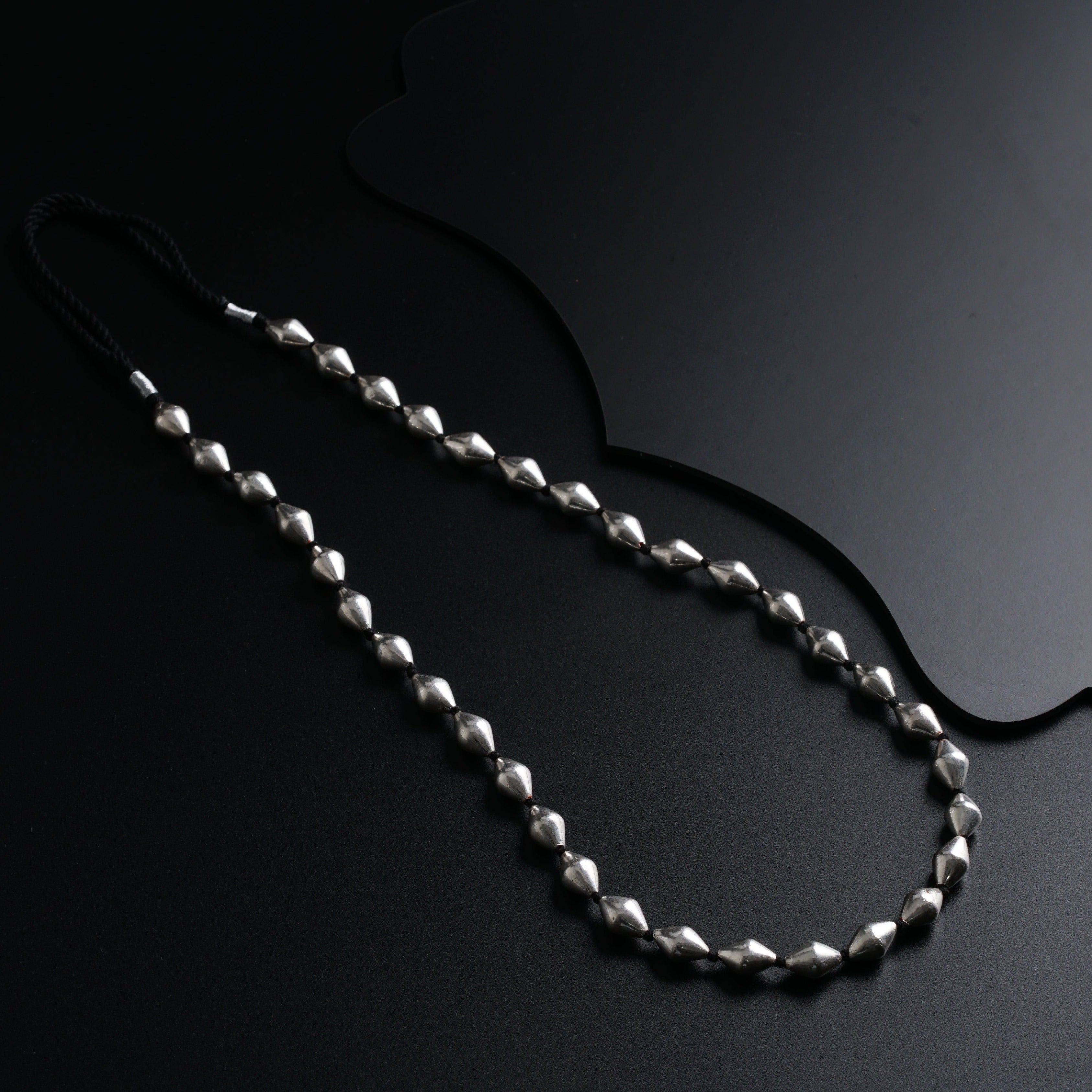 a long silver beaded necklace on a black surface