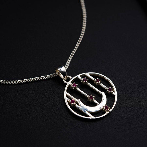a silver necklace with a silver circle and a red bead on it