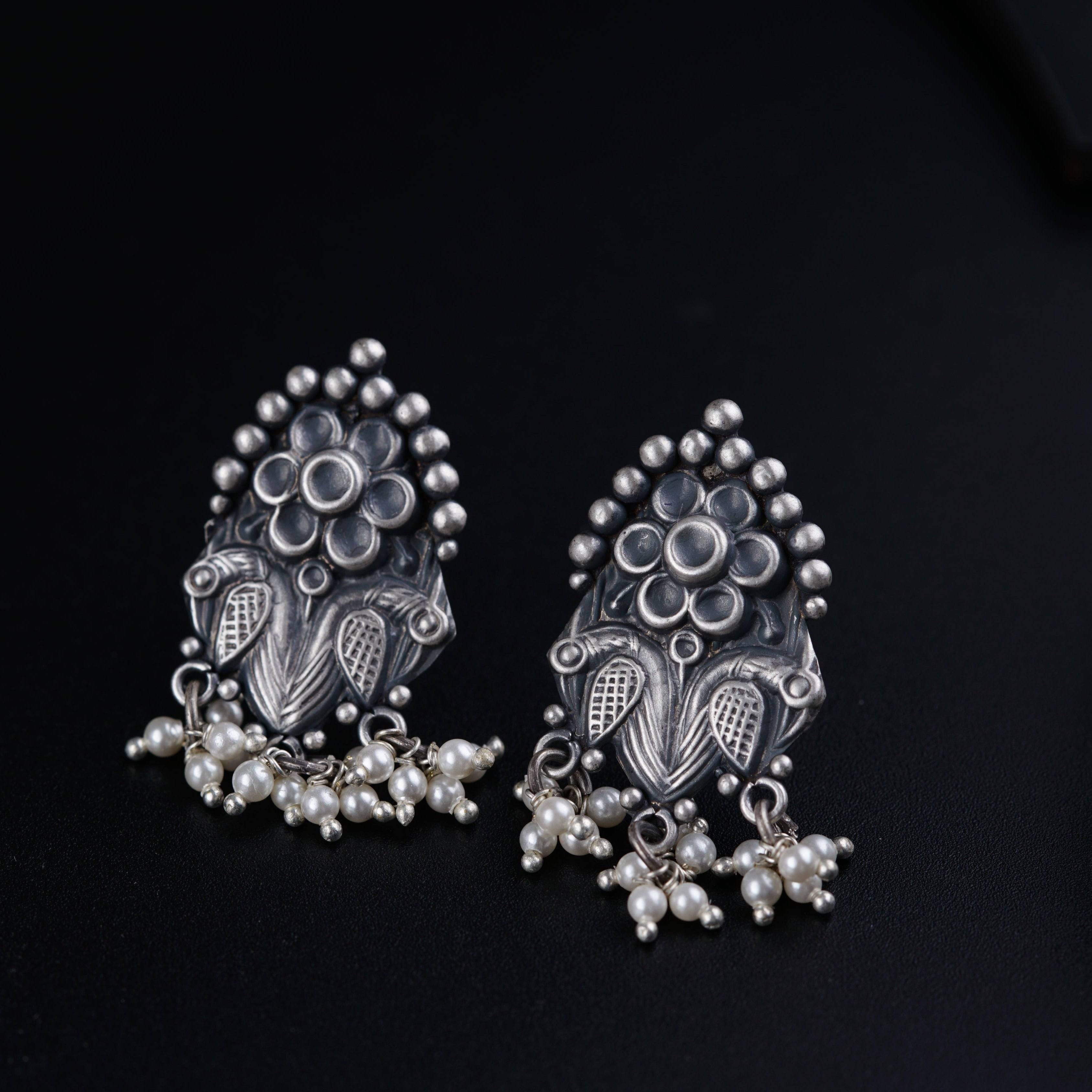 a pair of silver earrings with pearls on a black background