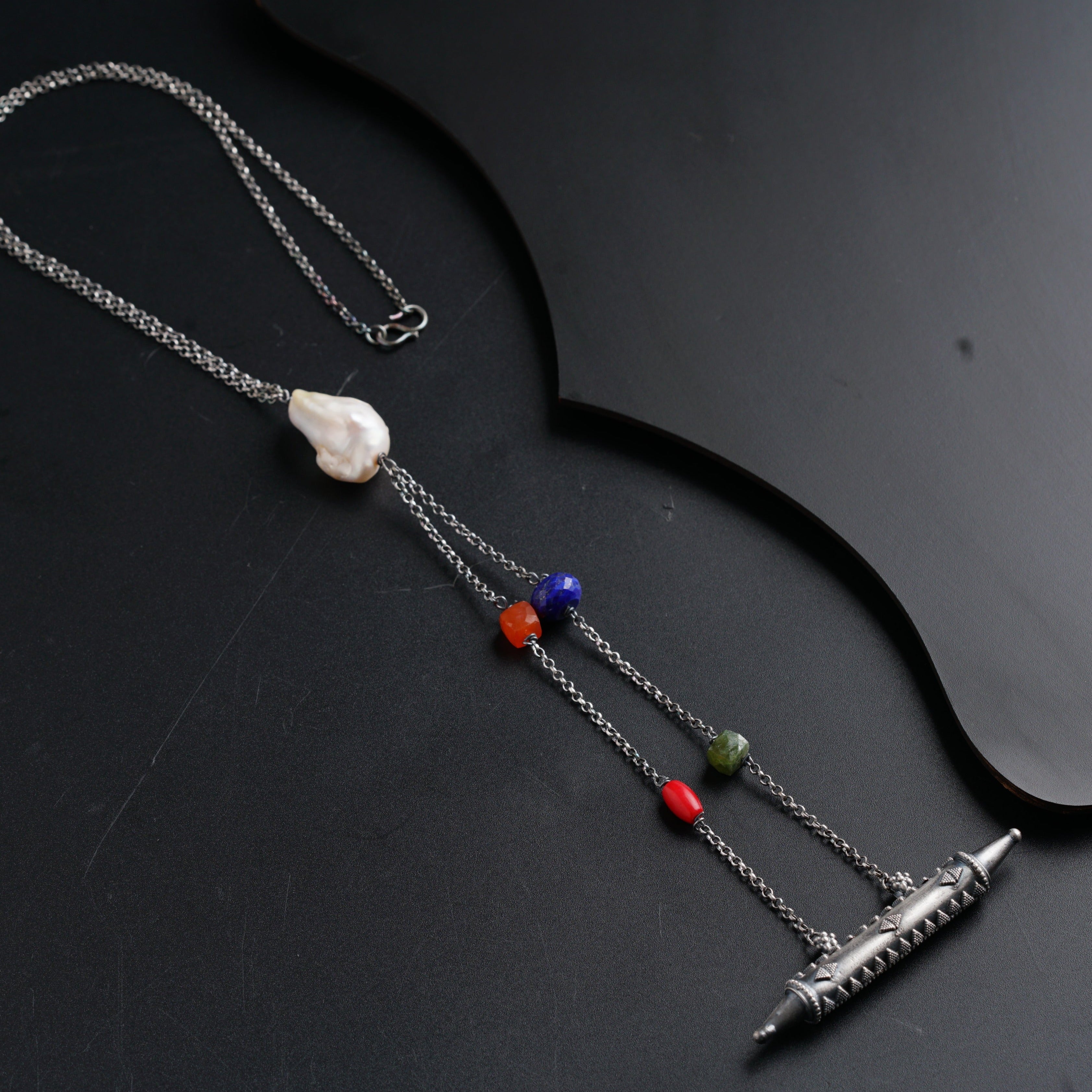 a necklace with beads and a pen on a black surface
