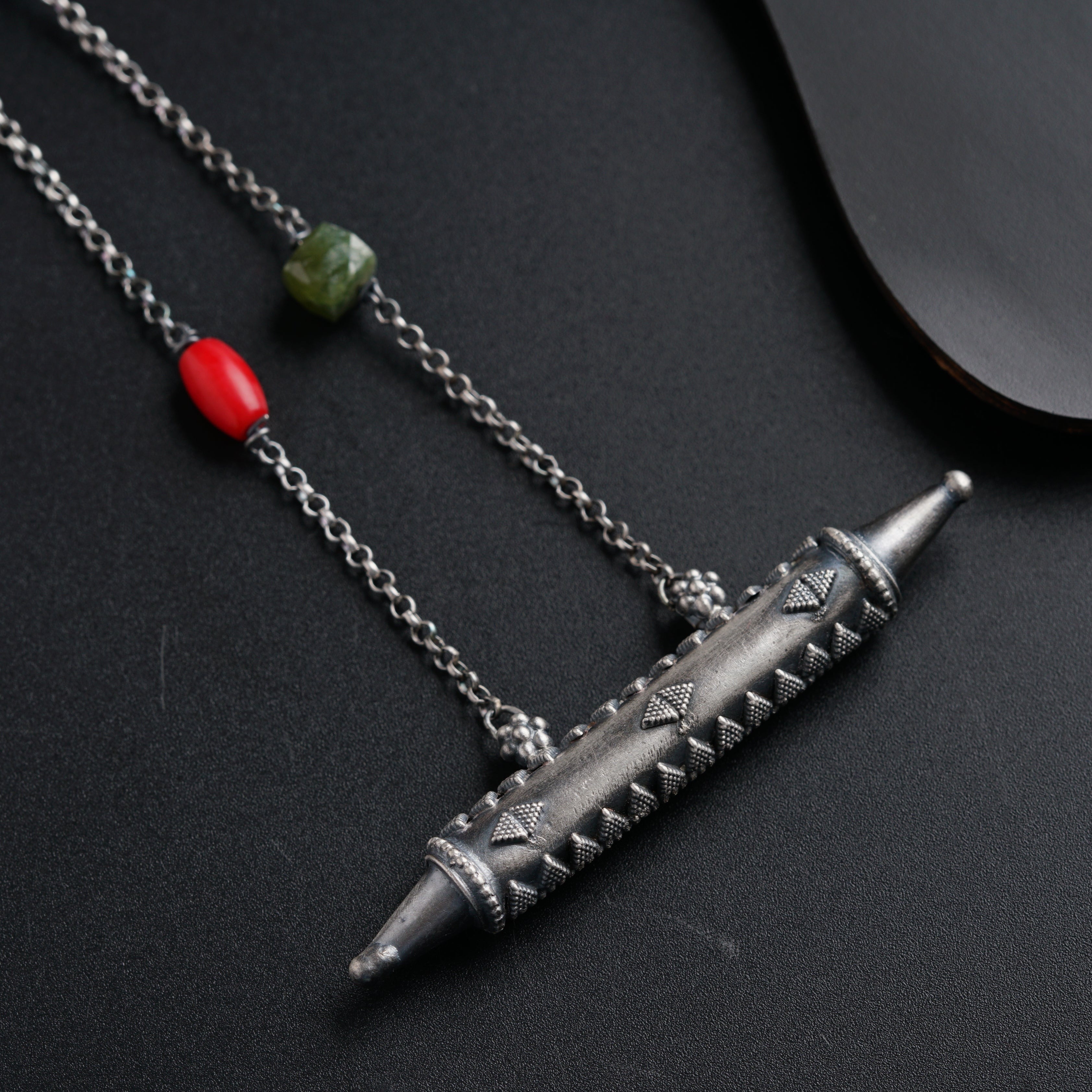 a silver necklace with a red bead on it