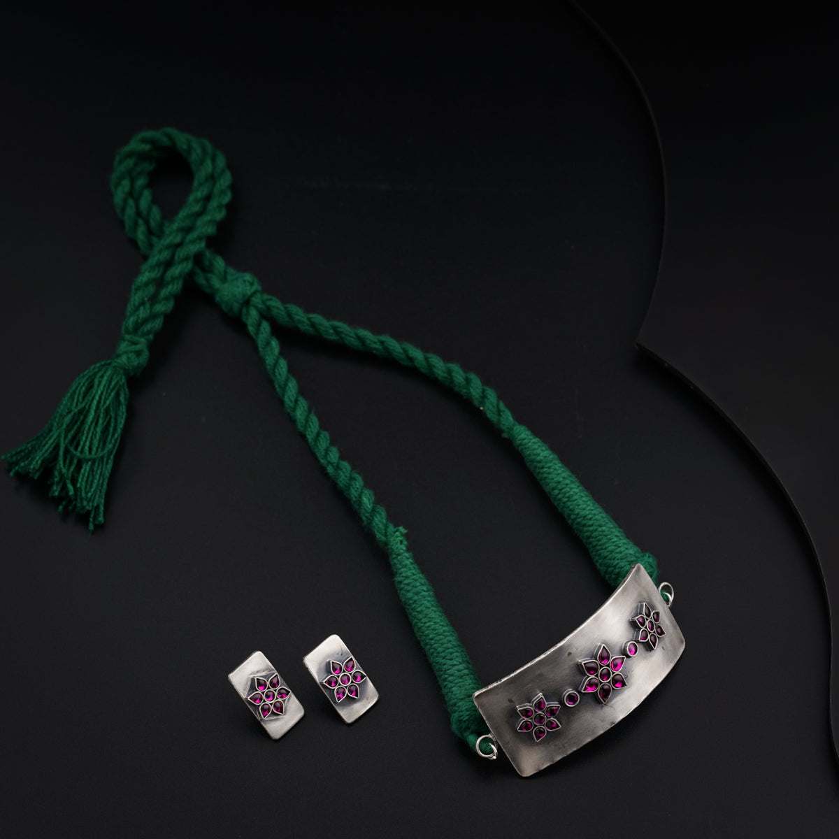 a pair of earrings and a green cord on a black surface