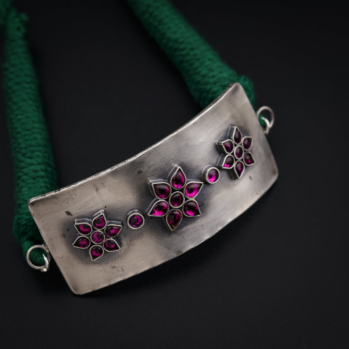 a silver bracelet with pink flowers on a green cord