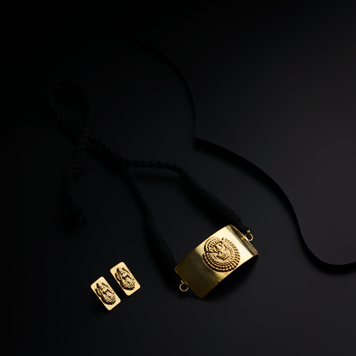 a black and gold necklace and two gold square pendants