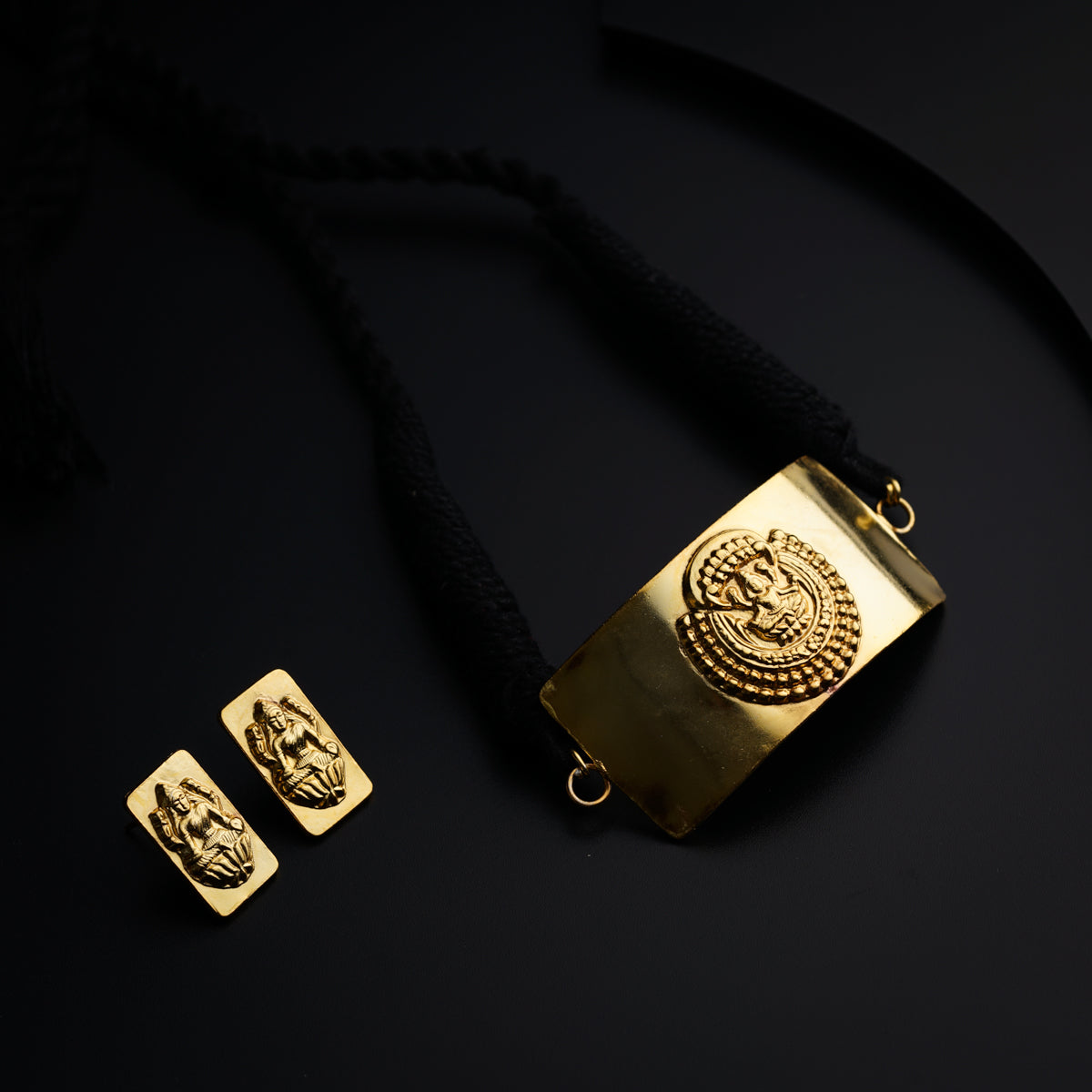 a gold necklace with two square pendants on a black background