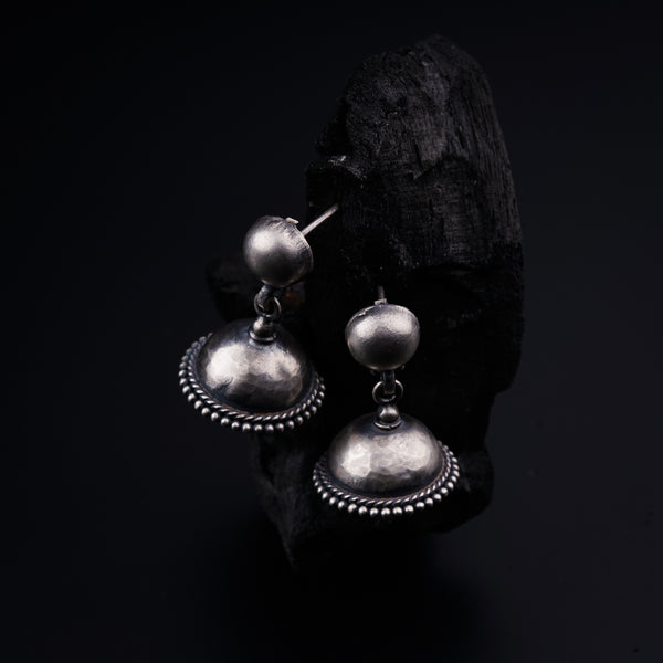 a pair of silver earrings sitting on top of a piece of wood