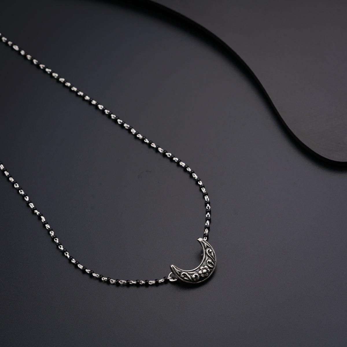 a silver necklace with a crescent on a black surface