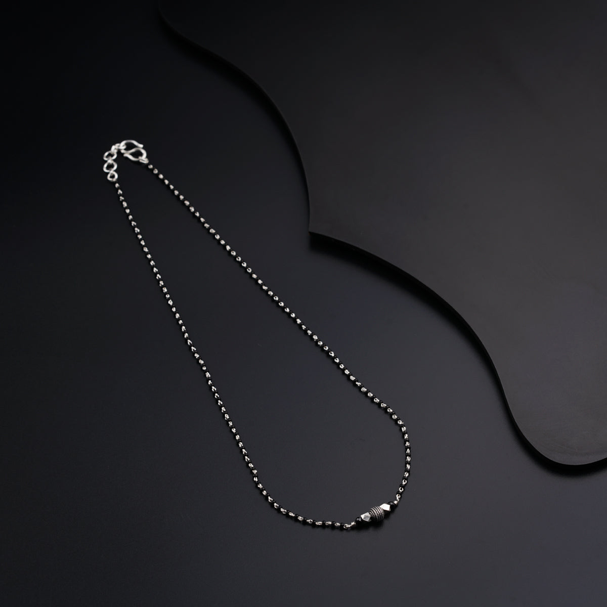 a silver necklace with a ball chain on a black background