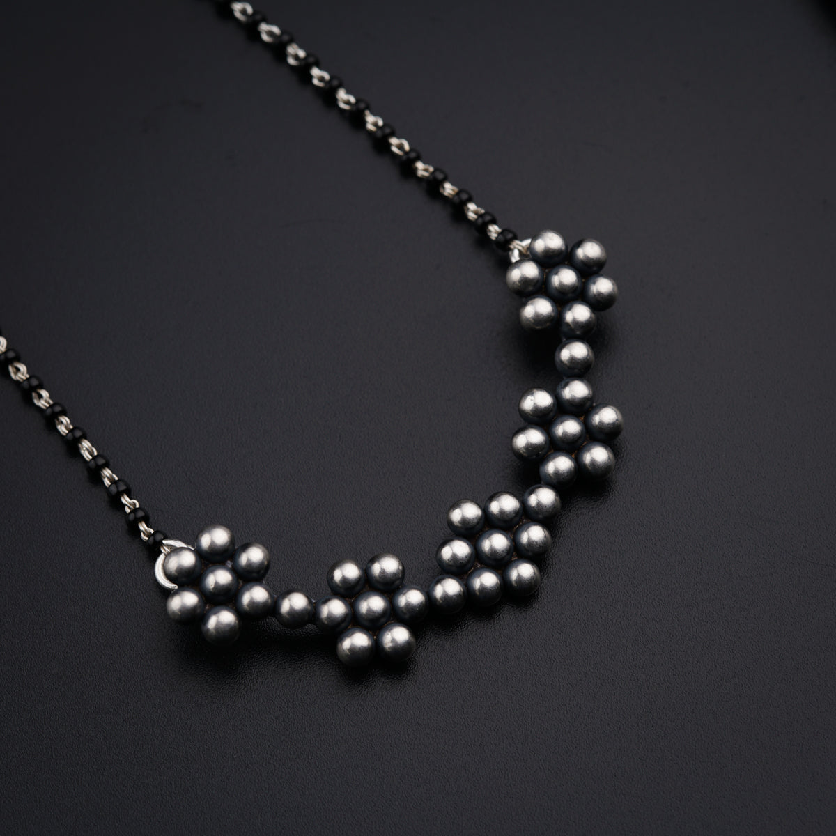 a necklace made of silver balls on a black surface