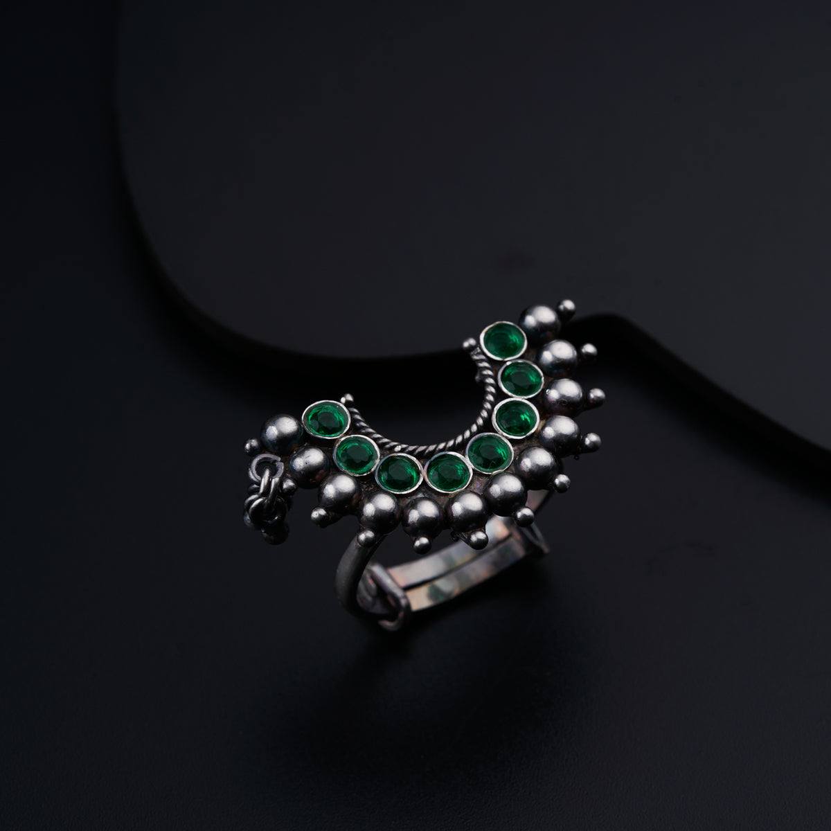 a silver ring with green stones on a black surface