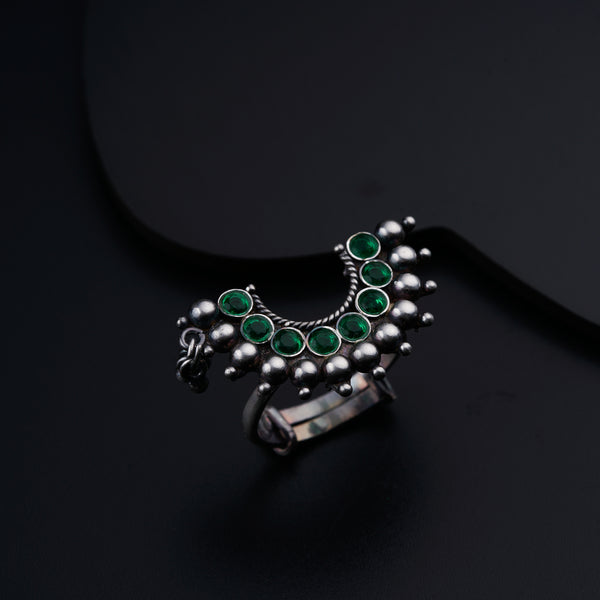 a silver ring with green stones on a black surface