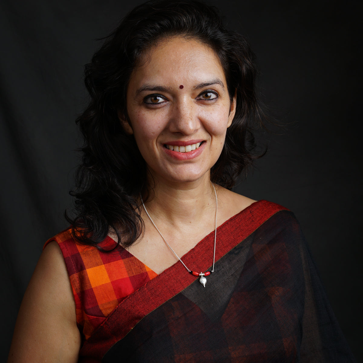 a woman in a red and black sari smiling