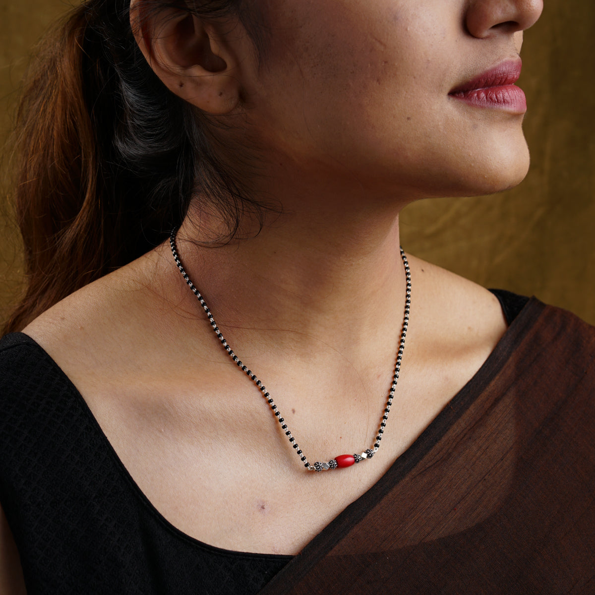 a woman wearing a necklace with a red bea