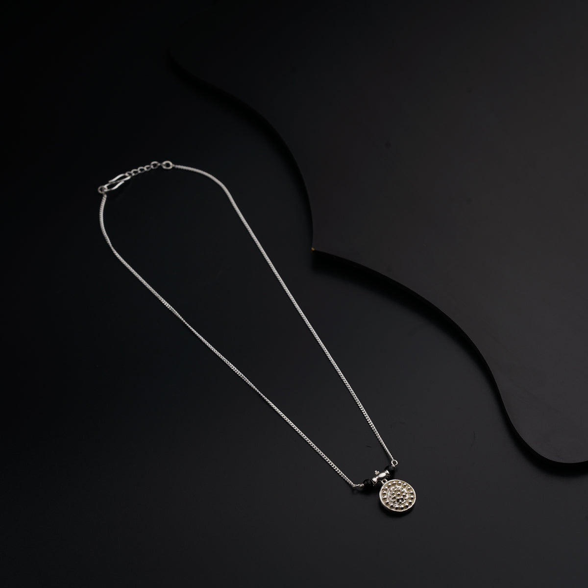 a silver necklace with a medallion on a black background