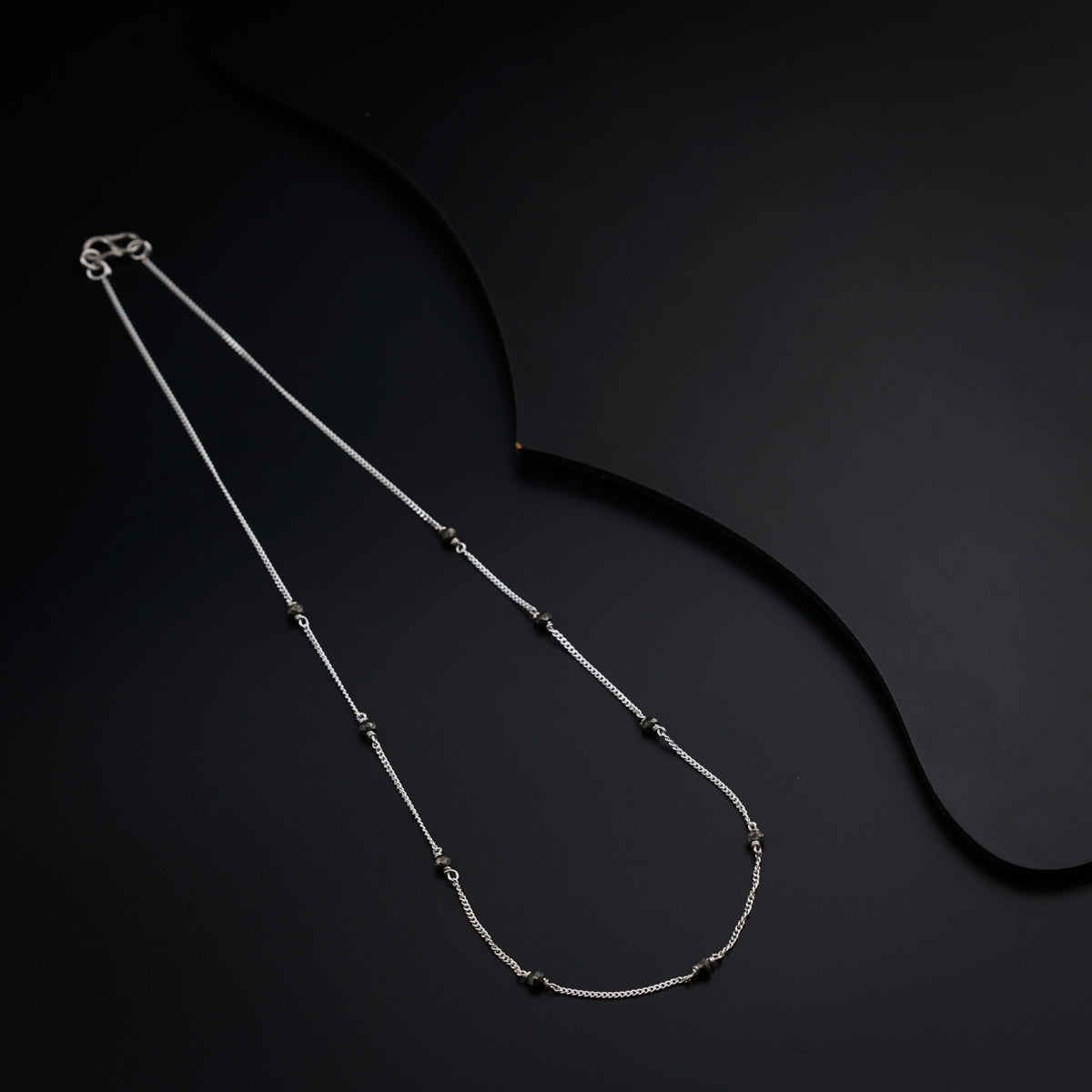 a silver necklace with a black bead on a black background