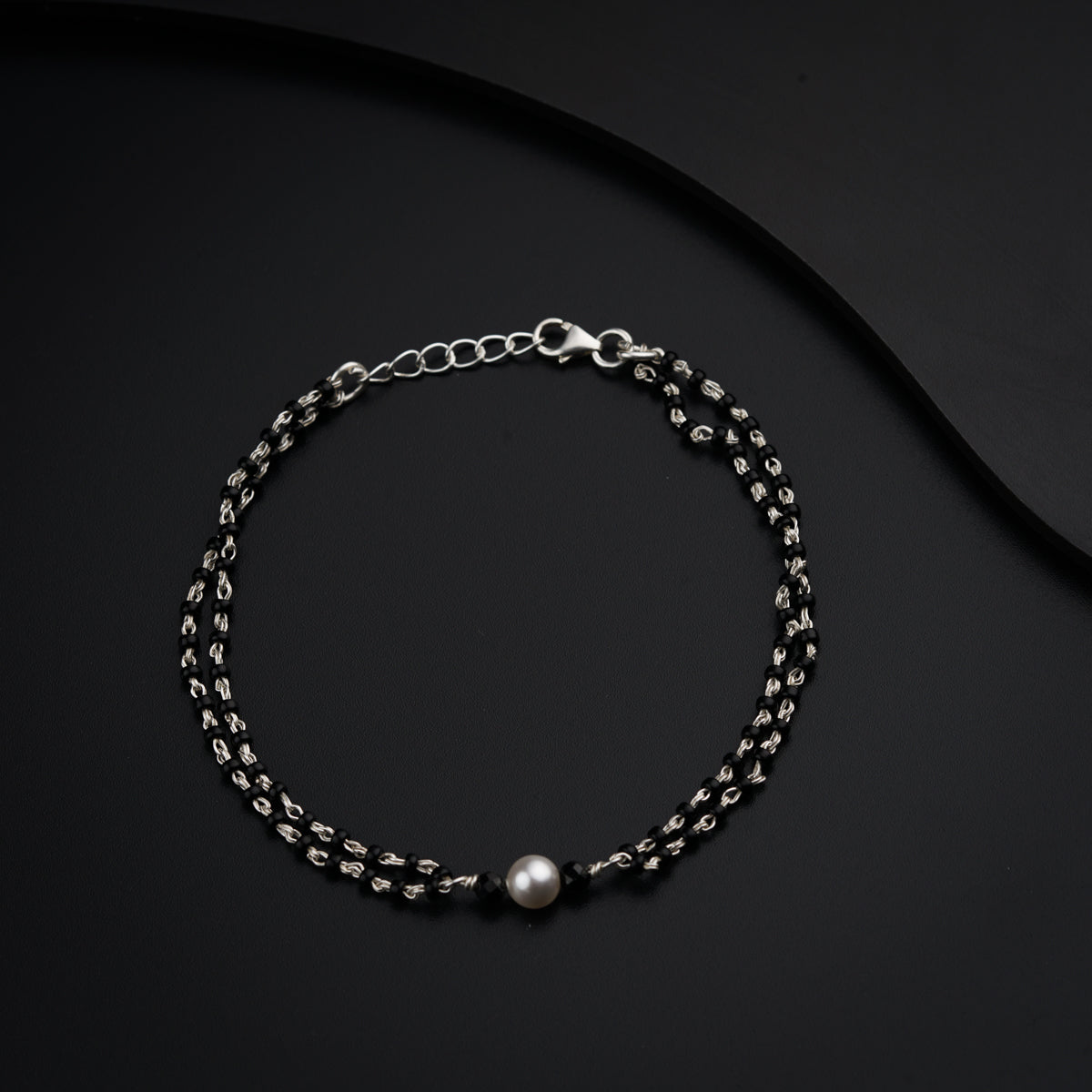 a silver bracelet with a pearl on a black background