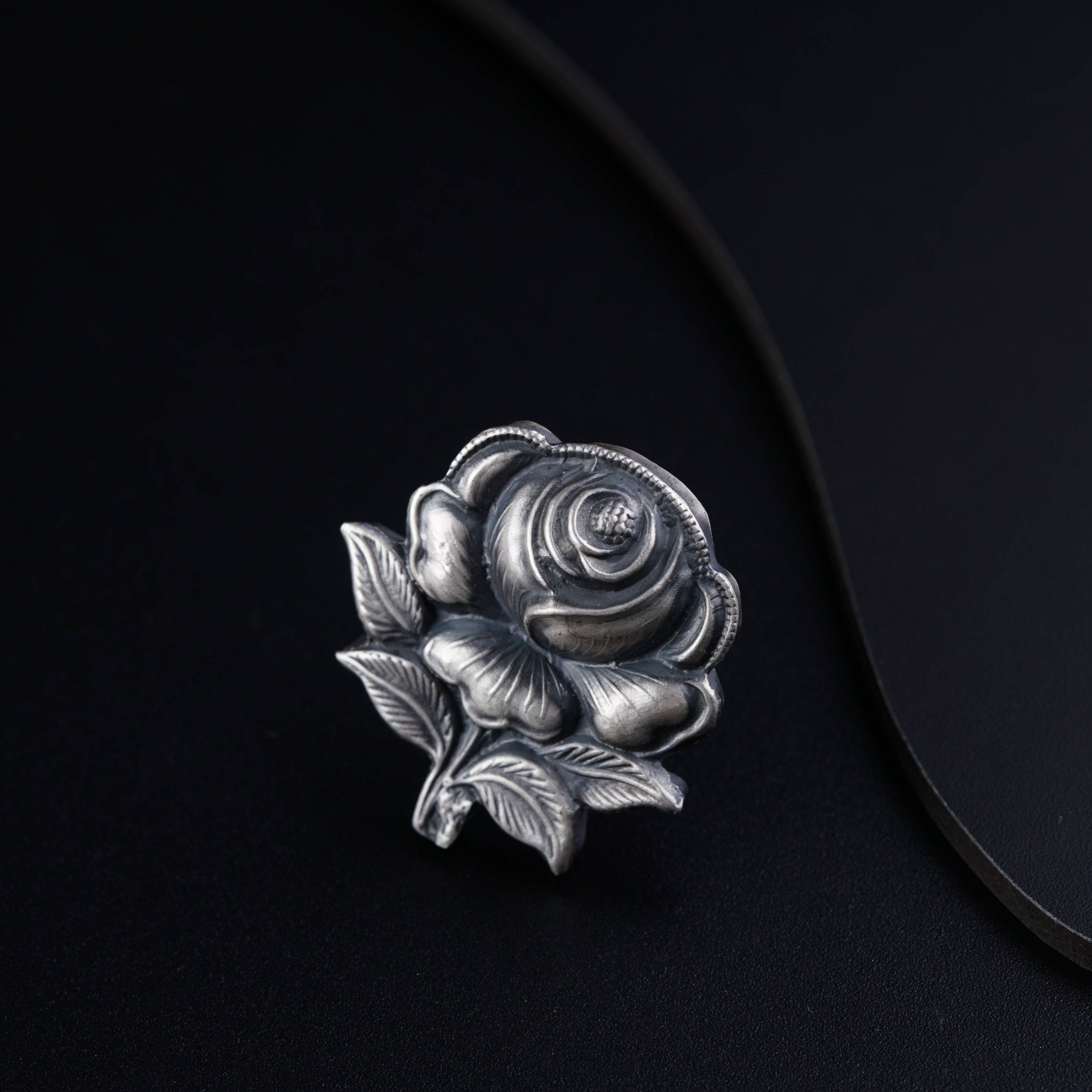 a silver rose brooch sitting on top of a black surface